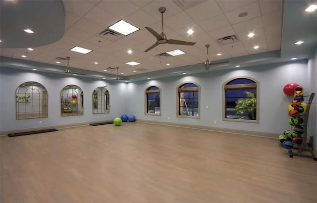 exercise room featuring ceiling fan, a drop ceiling, and light wood-type flooring