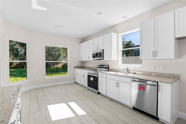 kitchen with light stone countertops, white cabinetry, sink, appliances with stainless steel finishes, and light wood-type flooring