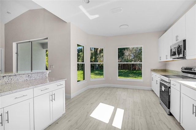 kitchen featuring vaulted ceiling, appliances with stainless steel finishes, light hardwood / wood-style floors, light stone counters, and white cabinetry