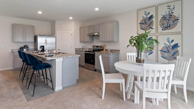 kitchen featuring appliances with stainless steel finishes, light colored carpet, gray cabinets, and a kitchen island with sink