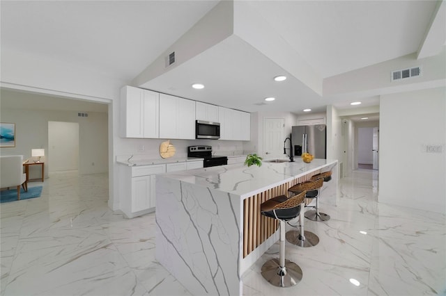 kitchen with white cabinetry, a kitchen bar, stainless steel appliances, and a center island with sink