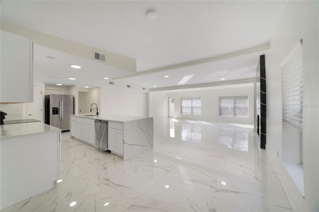 kitchen featuring sink, appliances with stainless steel finishes, a kitchen island with sink, light stone countertops, and white cabinets