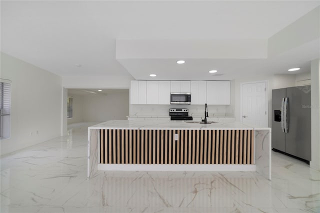 kitchen with appliances with stainless steel finishes, white cabinetry, sink, light stone countertops, and a center island with sink