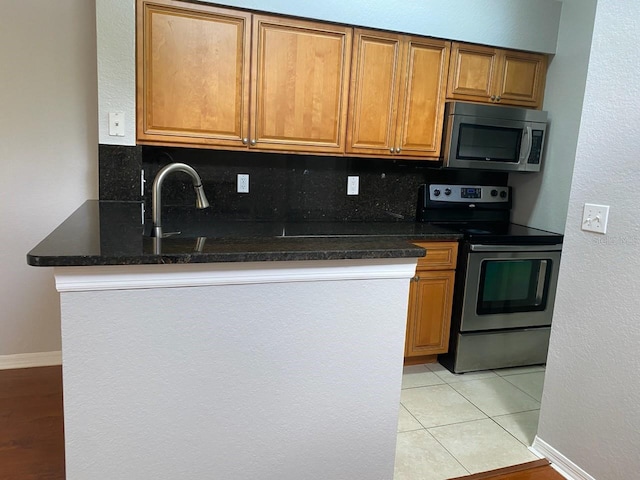 kitchen featuring decorative backsplash, appliances with stainless steel finishes, light tile patterned floors, and dark stone counters