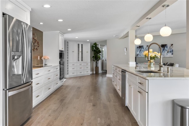 kitchen with light stone countertops, stainless steel appliances, sink, decorative light fixtures, and white cabinets