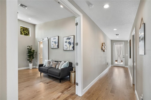 corridor featuring a barn door, light hardwood / wood-style floors, and a textured ceiling