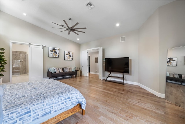 bedroom with connected bathroom, light hardwood / wood-style floors, lofted ceiling, and a barn door