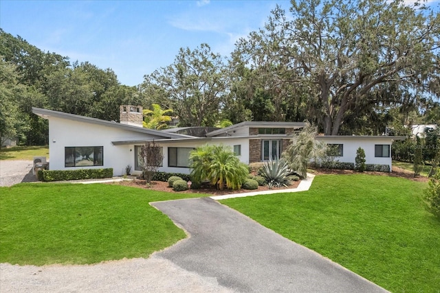 12550 Lakeshore Dr, Clermont, FL 34711 - mid-century modern home featuring a front yard, a chimney, stucco siding, and asphalt driveway