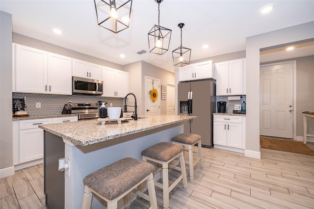 kitchen with a breakfast bar, stainless steel appliances, white cabinetry, and a kitchen island with sink