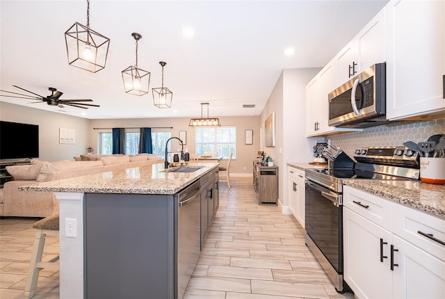 kitchen featuring appliances with stainless steel finishes, sink, pendant lighting, white cabinetry, and an island with sink