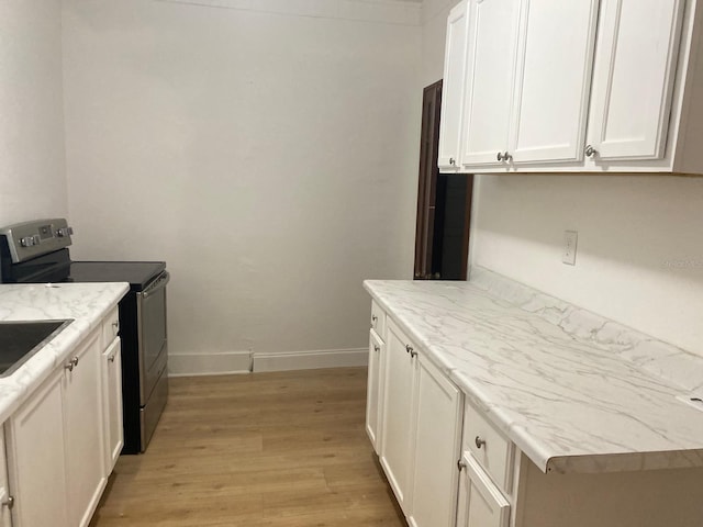 kitchen featuring electric stove, white cabinetry, light stone counters, and light wood-type flooring