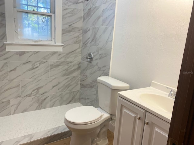 bathroom with toilet, a tile shower, tile walls, and vanity