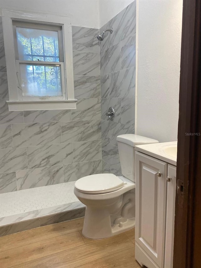 bathroom with vanity, toilet, a tile shower, and wood-type flooring