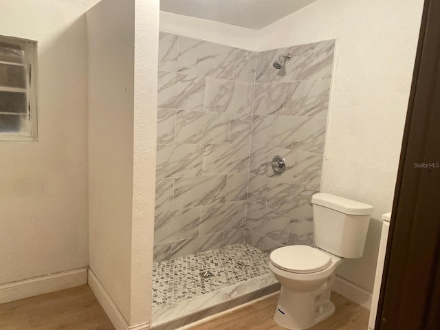 bathroom featuring toilet, a tile shower, and wood-type flooring