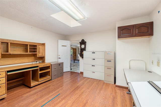 home office featuring a skylight, light hardwood / wood-style floors, and a textured ceiling