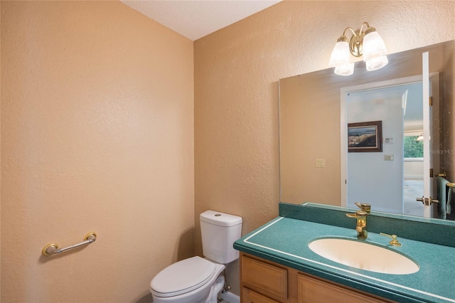 half bath with an inviting chandelier, toilet, vanity, and a textured wall