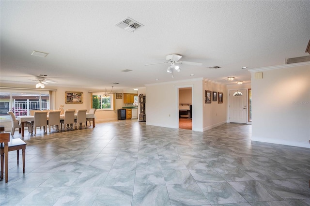 unfurnished living room with visible vents, ornamental molding, a textured ceiling, and ceiling fan