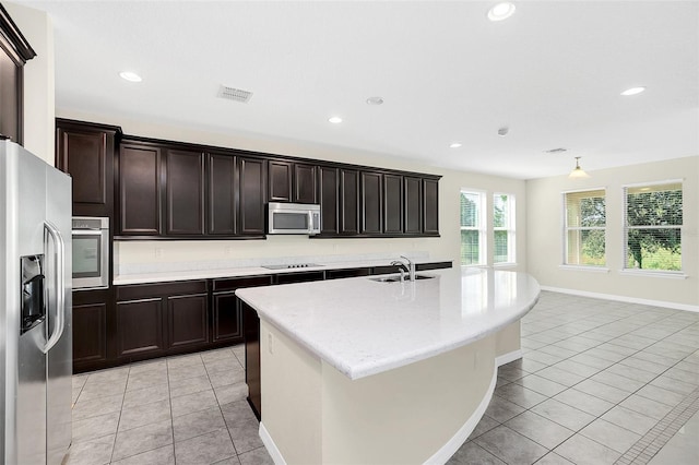 kitchen featuring sink, light tile patterned floors, stainless steel appliances, and an island with sink