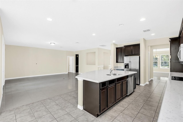 kitchen with dark brown cabinets, stainless steel appliances, sink, an island with sink, and light tile patterned flooring