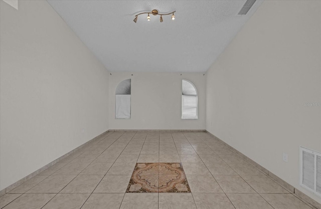 empty room featuring a textured ceiling, vaulted ceiling, and light tile patterned flooring