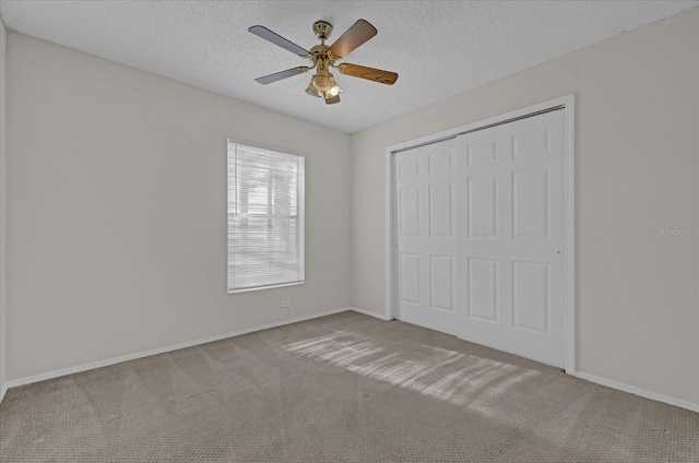 unfurnished bedroom featuring ceiling fan, light colored carpet, a textured ceiling, and a closet