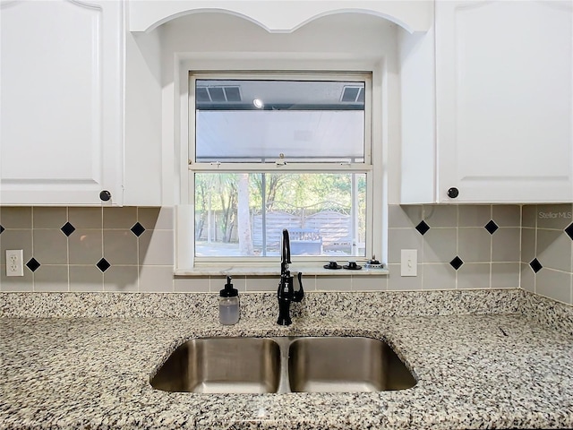 kitchen featuring backsplash, white cabinetry, sink, and light stone counters