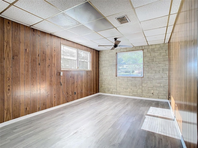 empty room with a paneled ceiling, ceiling fan, wooden walls, and hardwood / wood-style flooring