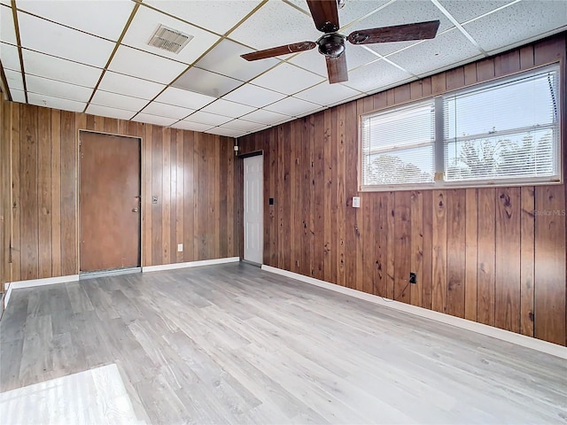 unfurnished room with a paneled ceiling, light hardwood / wood-style flooring, ceiling fan, and wood walls