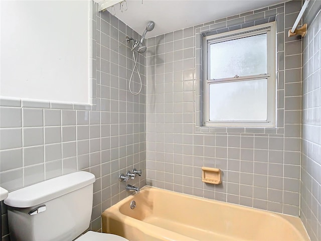 bathroom with toilet, tiled shower / bath, and tile walls