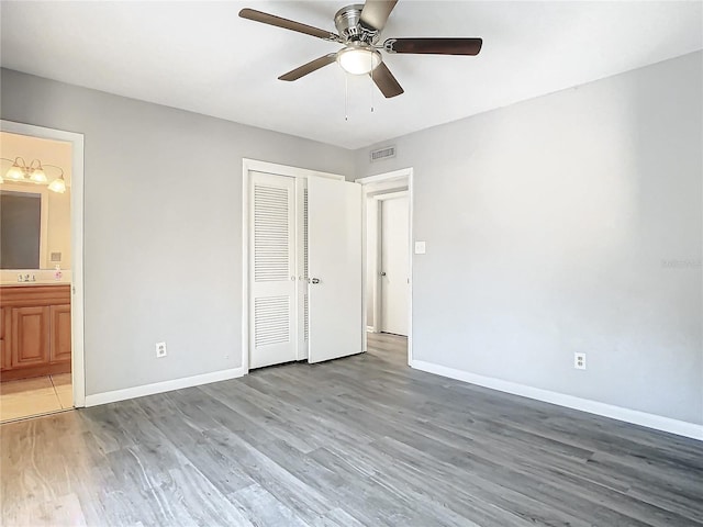 unfurnished bedroom with ensuite bathroom, a closet, ceiling fan, and hardwood / wood-style flooring