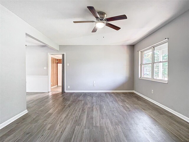 empty room with ceiling fan, baseboards, dark wood finished floors, and beamed ceiling