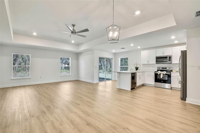 kitchen featuring white cabinets, kitchen peninsula, stainless steel appliances, and a tray ceiling