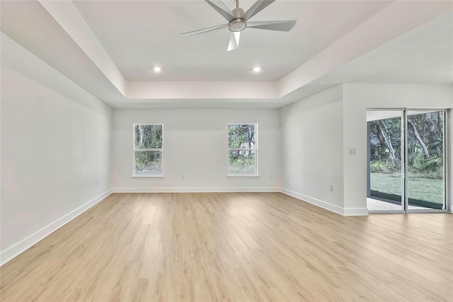 spare room featuring a raised ceiling, ceiling fan, and light hardwood / wood-style flooring