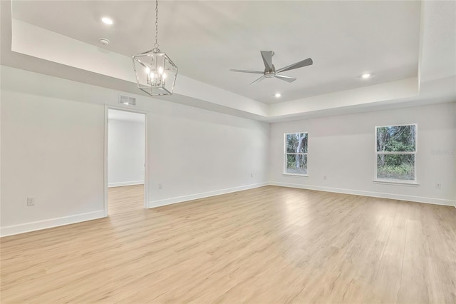 empty room featuring ceiling fan with notable chandelier, light wood-type flooring, and a raised ceiling