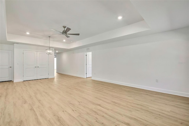 interior space with ceiling fan with notable chandelier, light wood-type flooring, and a tray ceiling