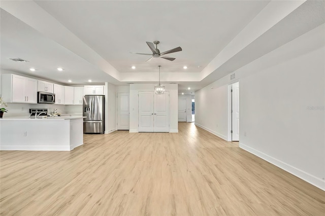 unfurnished living room with a raised ceiling, ceiling fan, and light hardwood / wood-style floors