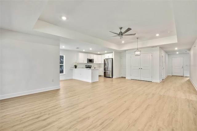 unfurnished living room with ceiling fan, a raised ceiling, and light wood-type flooring