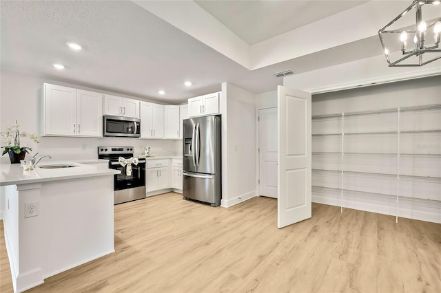 kitchen with white cabinets, hanging light fixtures, light hardwood / wood-style flooring, kitchen peninsula, and stainless steel appliances