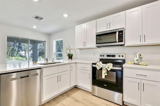 kitchen with sink, white cabinetry, stainless steel appliances, and light hardwood / wood-style flooring