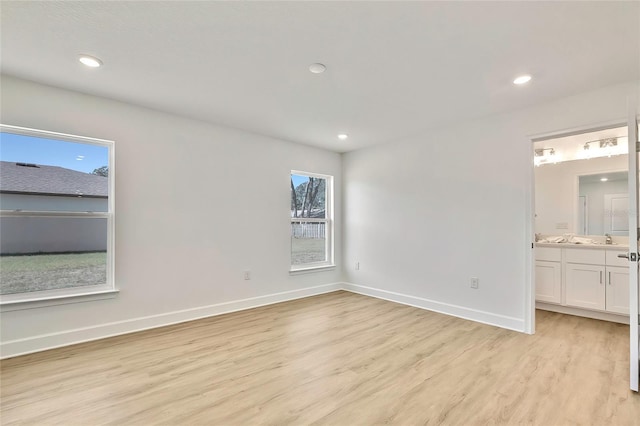 unfurnished bedroom with ensuite bathroom, sink, light hardwood / wood-style flooring, and multiple windows