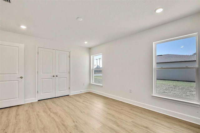 unfurnished bedroom with a closet, light hardwood / wood-style flooring, and multiple windows