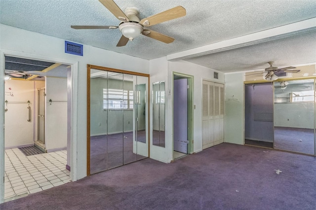 unfurnished bedroom with a textured ceiling, carpet floors, two closets, and ceiling fan