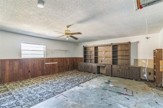 unfurnished room with ceiling fan, wood walls, a textured ceiling, and concrete floors