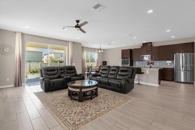 living room with ceiling fan with notable chandelier and light wood-type flooring