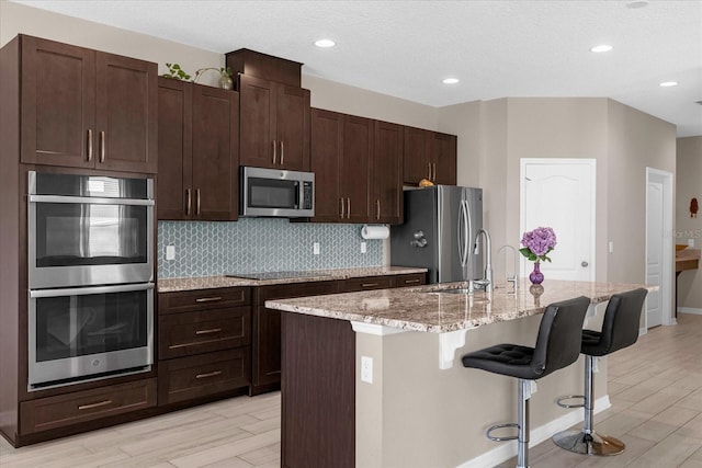 kitchen featuring a center island with sink, a kitchen breakfast bar, stainless steel appliances, and light hardwood / wood-style flooring