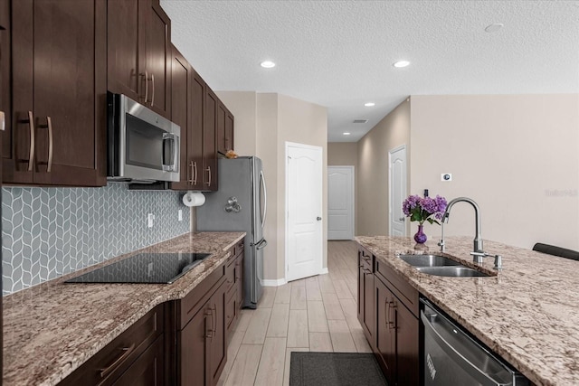 kitchen featuring sink, tasteful backsplash, light stone counters, dark brown cabinets, and appliances with stainless steel finishes