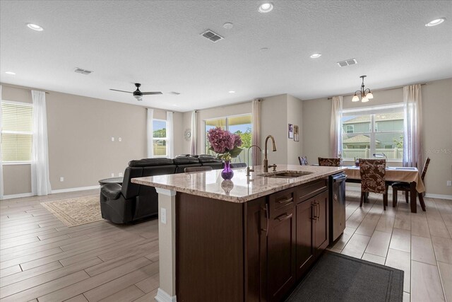 kitchen featuring sink, stainless steel dishwasher, light stone countertops, an island with sink, and light hardwood / wood-style floors