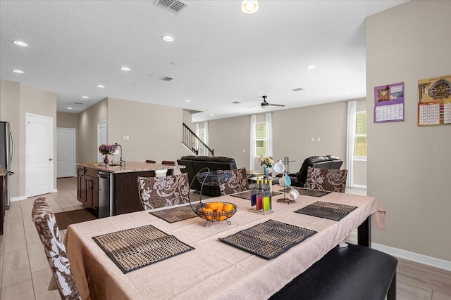 dining space featuring ceiling fan, sink, a textured ceiling, and light wood-type flooring