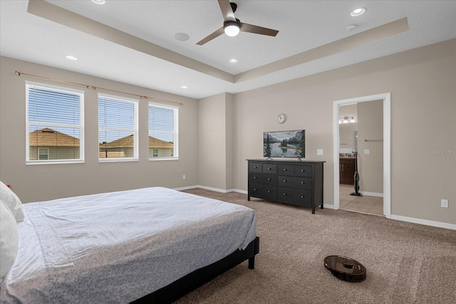 bedroom featuring a tray ceiling, ceiling fan, light colored carpet, and ensuite bathroom