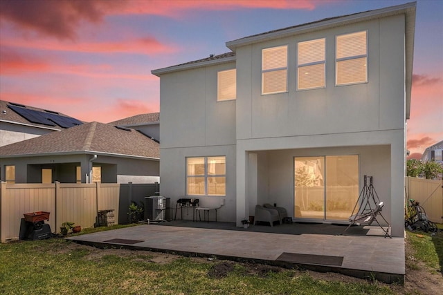 back house at dusk featuring a yard, a patio area, and central air condition unit